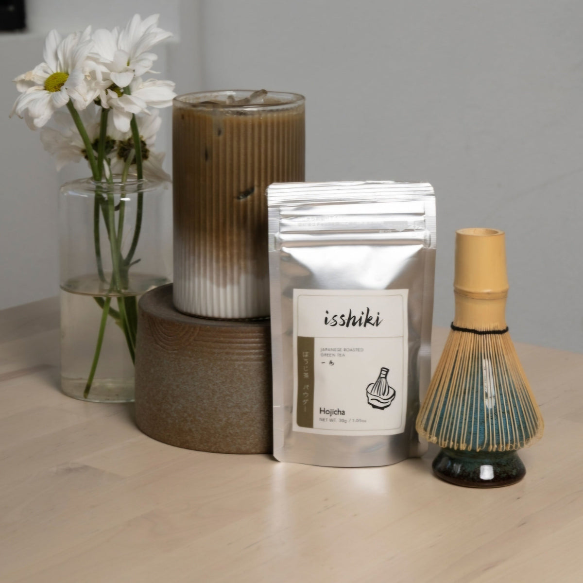 Hojicha roasted green tea powder isshiki beside a daisy vase and bamboo whisk on Tampa Home & Garden Store