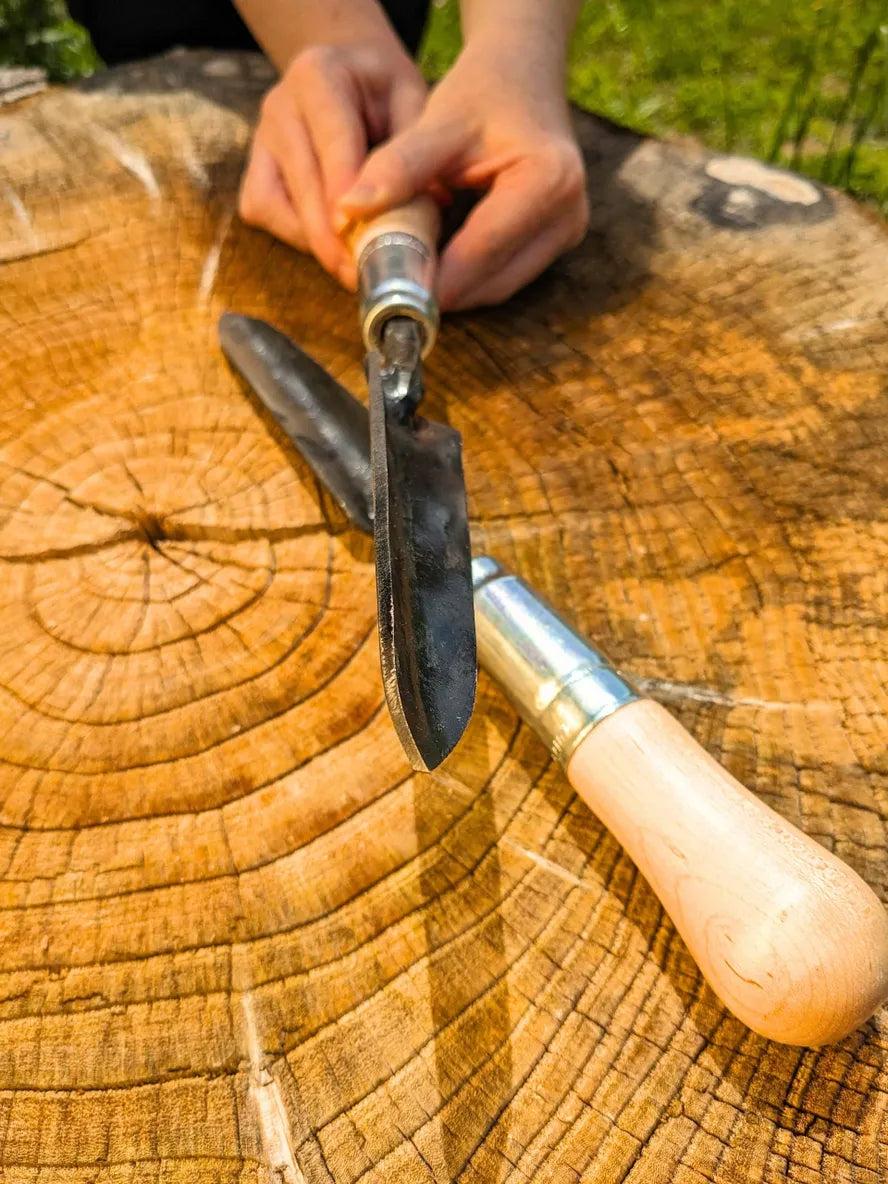 Sharp Shooter Trowel from Homestead Iron, LLC with wooden handle and black blade on a stump on Tampa Home & Garden Store