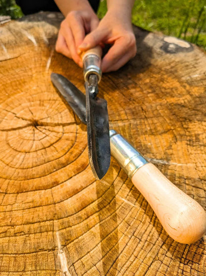 Sharp Shooter Trowel from Homestead Iron, LLC with wooden handle and black blade on a stump on Tampa Home & Garden Store