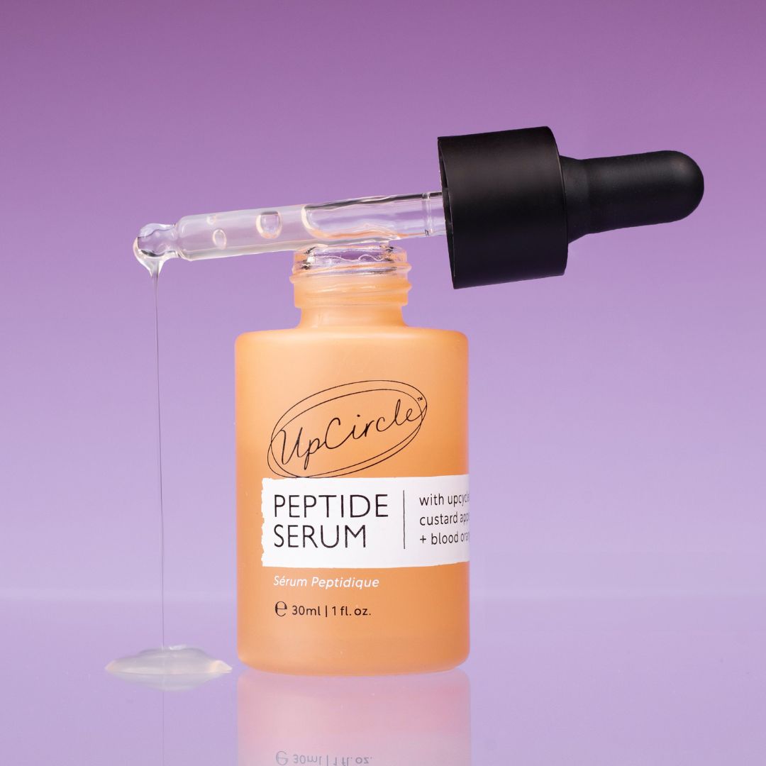 UpCircle peptide serum bottle with glass dropper, orange bottle and black cap on a purple background on Tampa Home & Garden Store