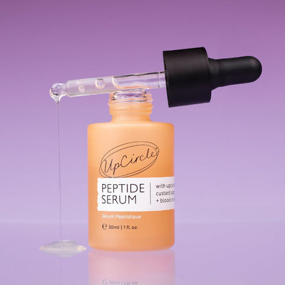 UpCircle peptide serum bottle with glass dropper, orange bottle and black cap on a purple background on Tampa Home & Garden Store