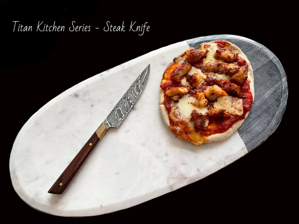Damascus steel steak knife with patterned blade and wooden handle beside pizza on board Titan on Tampa Home & Garden Store