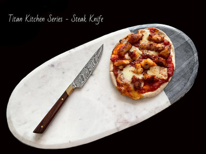 Damascus steel steak knife with patterned blade and wooden handle beside pizza on board Titan on Tampa Home & Garden Store