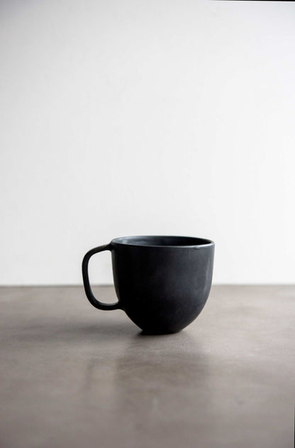 Black matte stoneware coffee mug by Creating Comfort with a curved handle on a gray surface on Tampa Home & Garden Store
