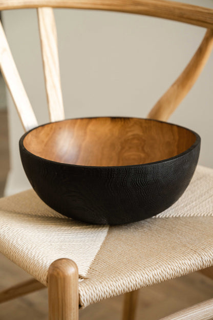 Hand Carved Large Half Charred Wooden Bowl with black exterior and warm wood interior on chair on Tampa Home & Garden Store