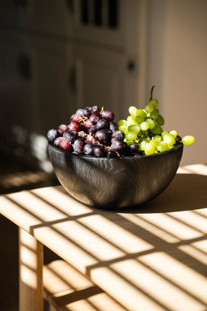 Hand carved half-charred black wooden bowl filled with red and green grapes on Tampa Home & Garden Store