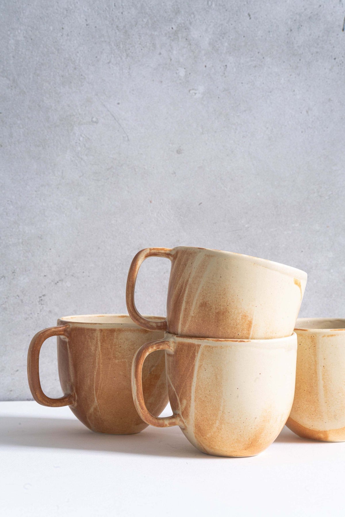 Stoneware beige coffee mugs by Creating Comfort; set of 4 with brown glaze, stacked on backdrop on Tampa Home & Garden Store