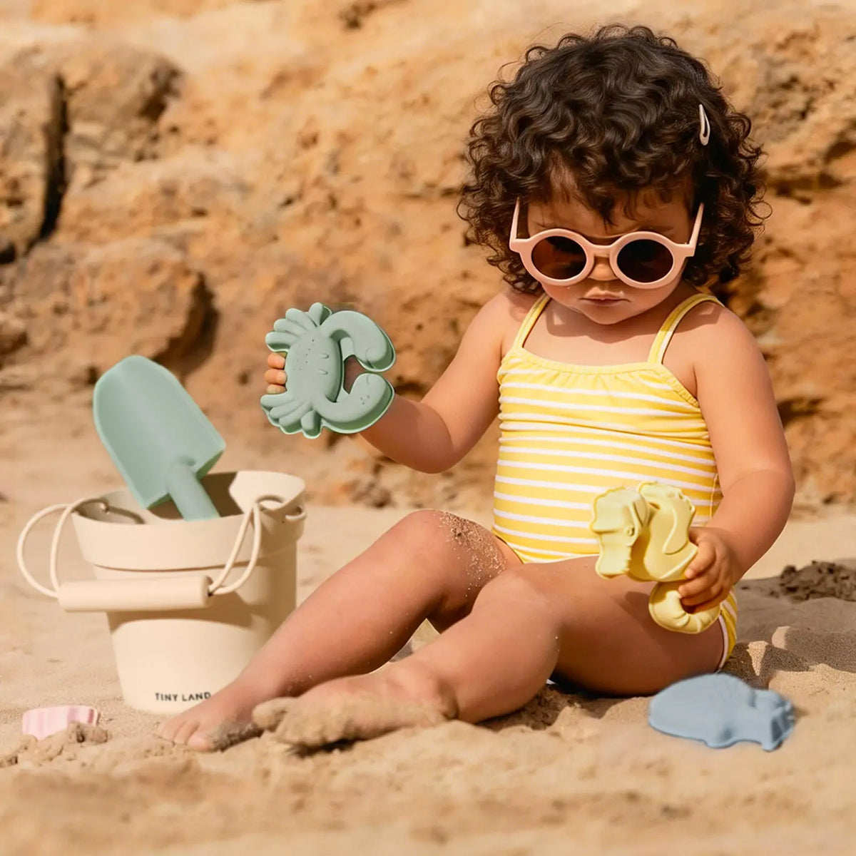 Tiny Land One-Stop Beach Toy & Tent Set toddler on beach with mint crab sand toy and Tiny Land bucket on Tampa Home & Garden Store