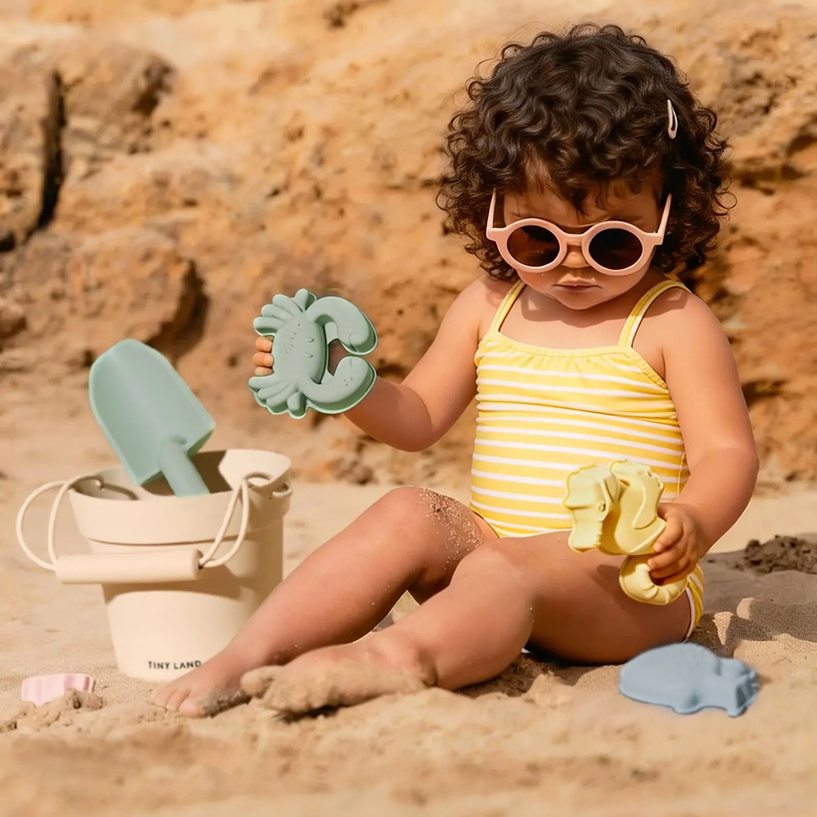 Tiny Land One-Stop Beach Toy & Tent Set toddler on beach with mint crab sand toy and Tiny Land bucket on Tampa Home & Garden Store