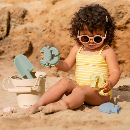 Tiny Land One-Stop Beach Toy & Tent Set toddler on beach with mint crab sand toy and Tiny Land bucket on Tampa Home & Garden Store