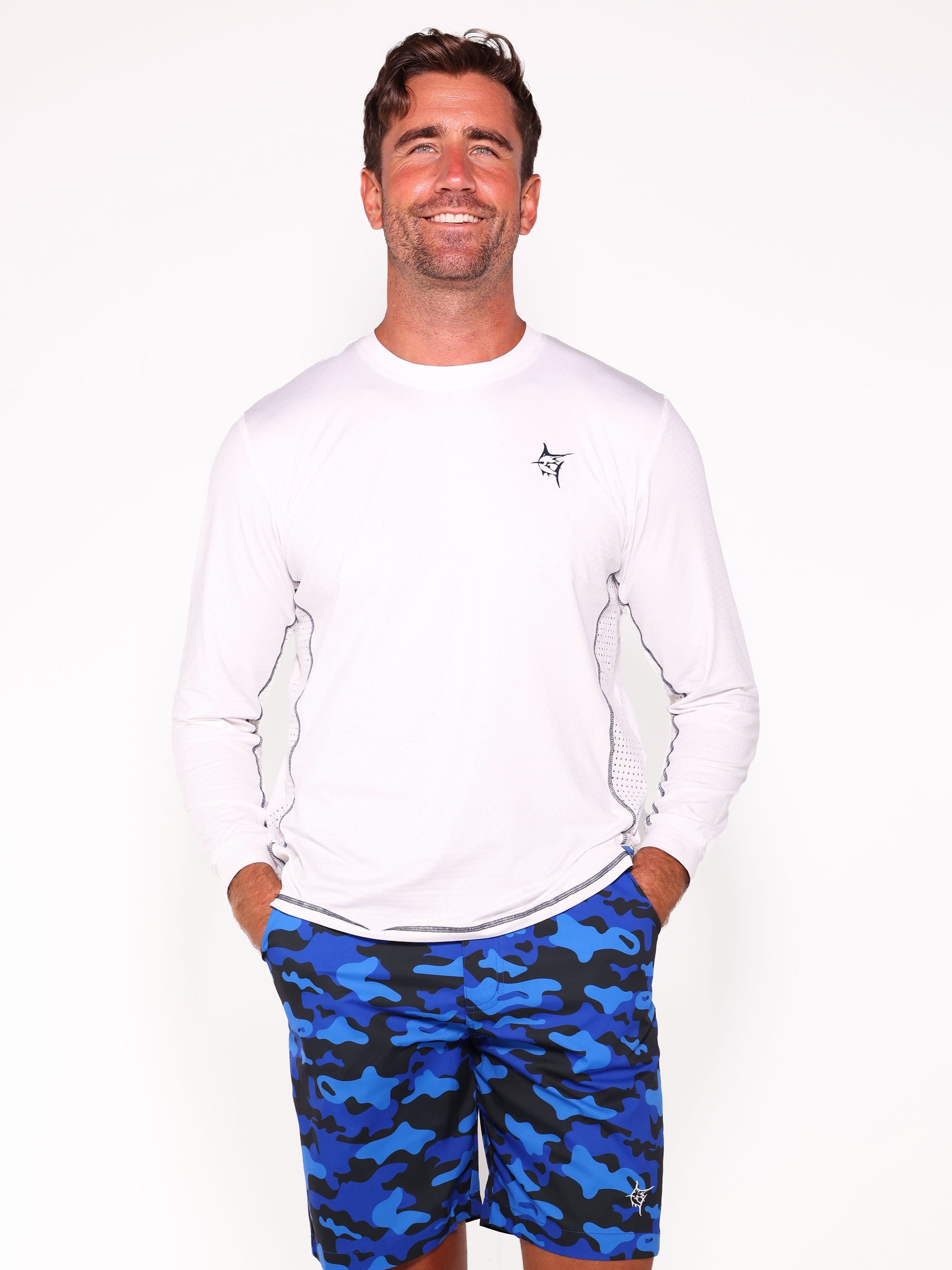 NautiFlex Performance Tee white long-sleeve with small navy chest logo, model wearing blue camouflage shorts on Tampa Home & Garden Store