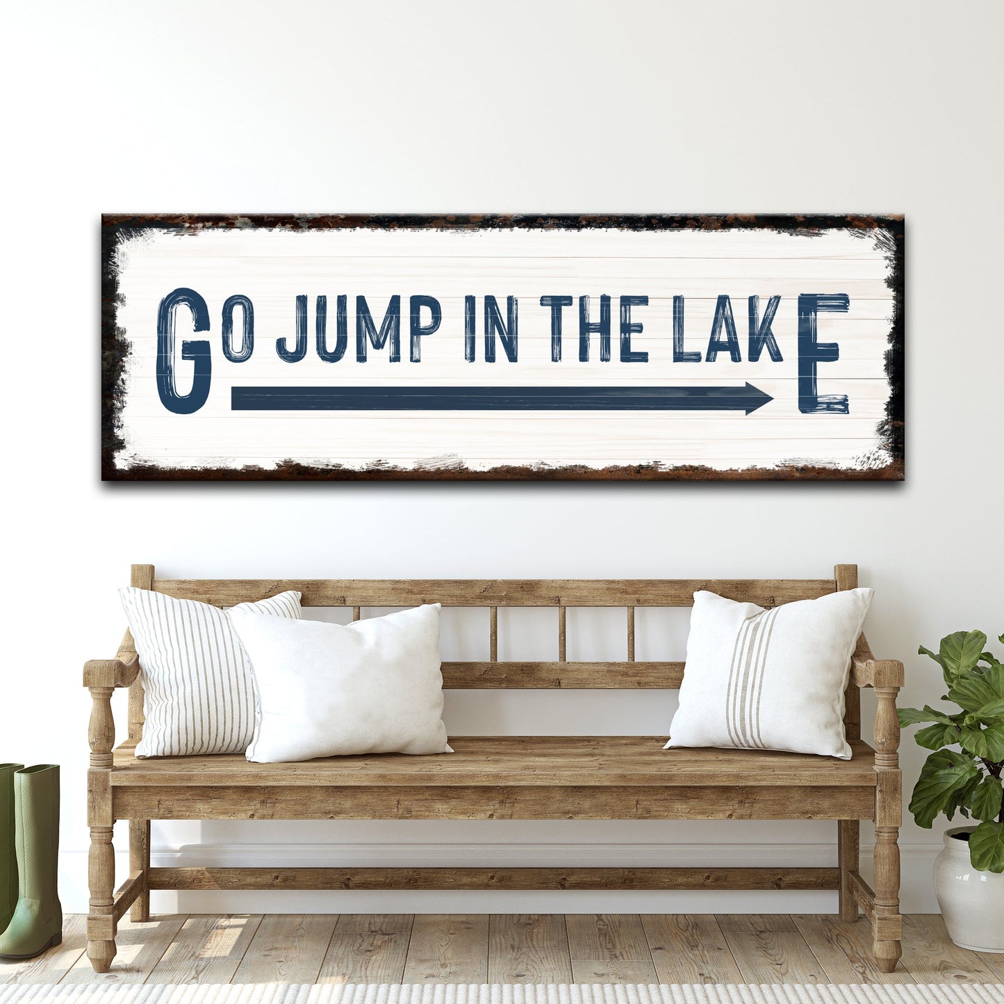 Go Jump In The Lake sign canvas with white plank background and distressed dark frame, bold blue lettering, above a rustic wooden bench on Tampa Home & Garden Store