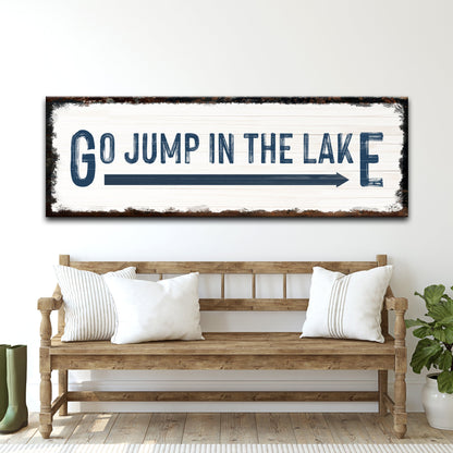 Go Jump In The Lake sign canvas with white plank background and distressed dark frame, bold blue lettering, above a rustic wooden bench on Tampa Home & Garden Store