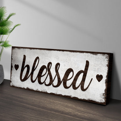 Blessed Sign canvas with distressed white panel and dark brown cursive lettering, shown beside a green palm plant on Tampa Home & Garden Store