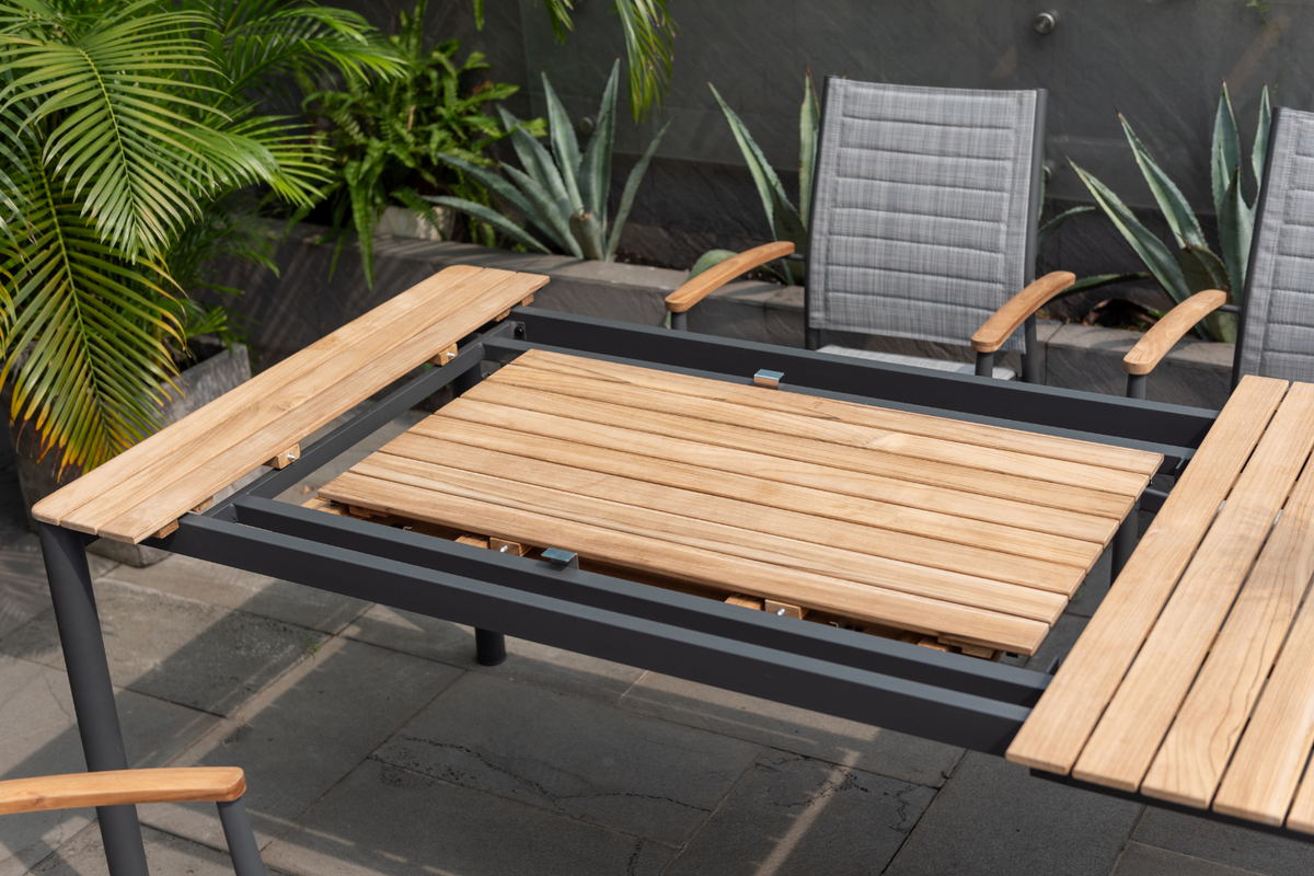 Topaz dark teak and aluminum rectangular extendable outdoor table with teak slats and extension leaves on a patio with gray outdoor chairs on Tampa Home & Garden Store