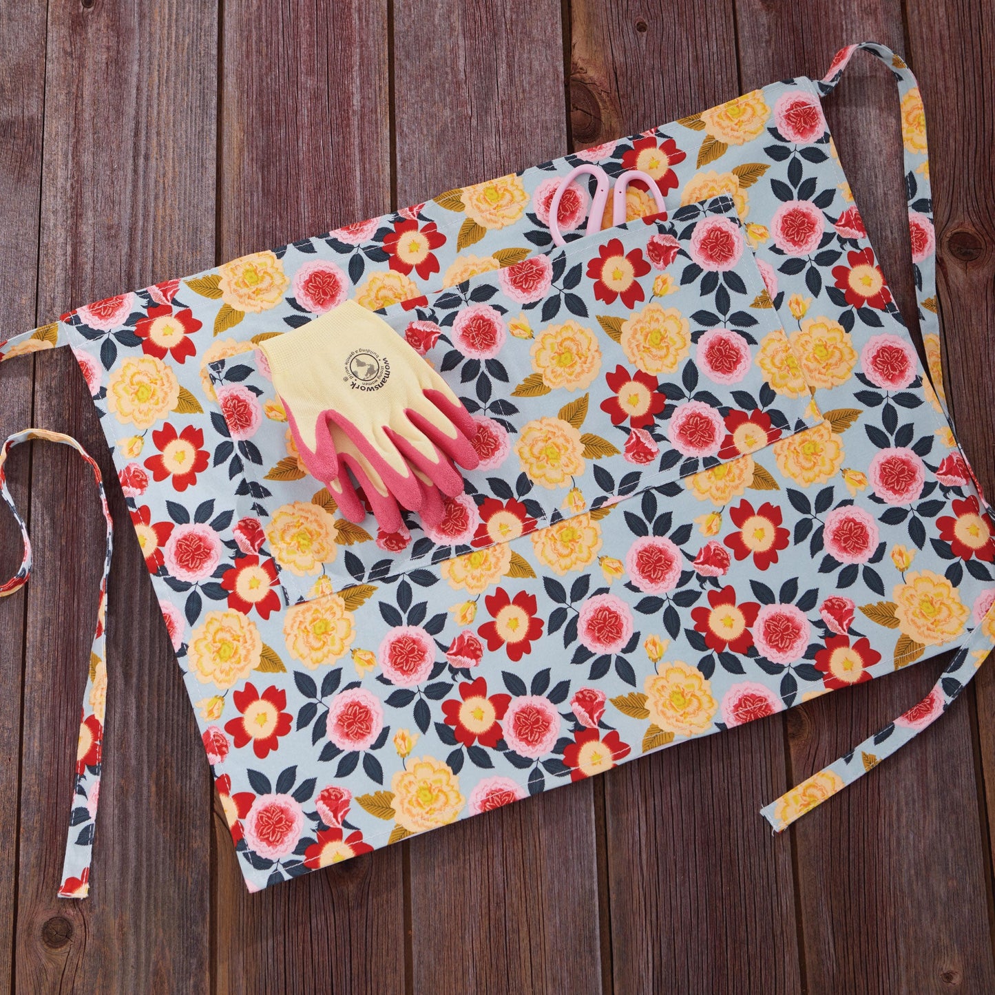 Gardener's Half Apron floral print by Womanswork on light blue fabric with pink gloves on Tampa Home & Garden Store