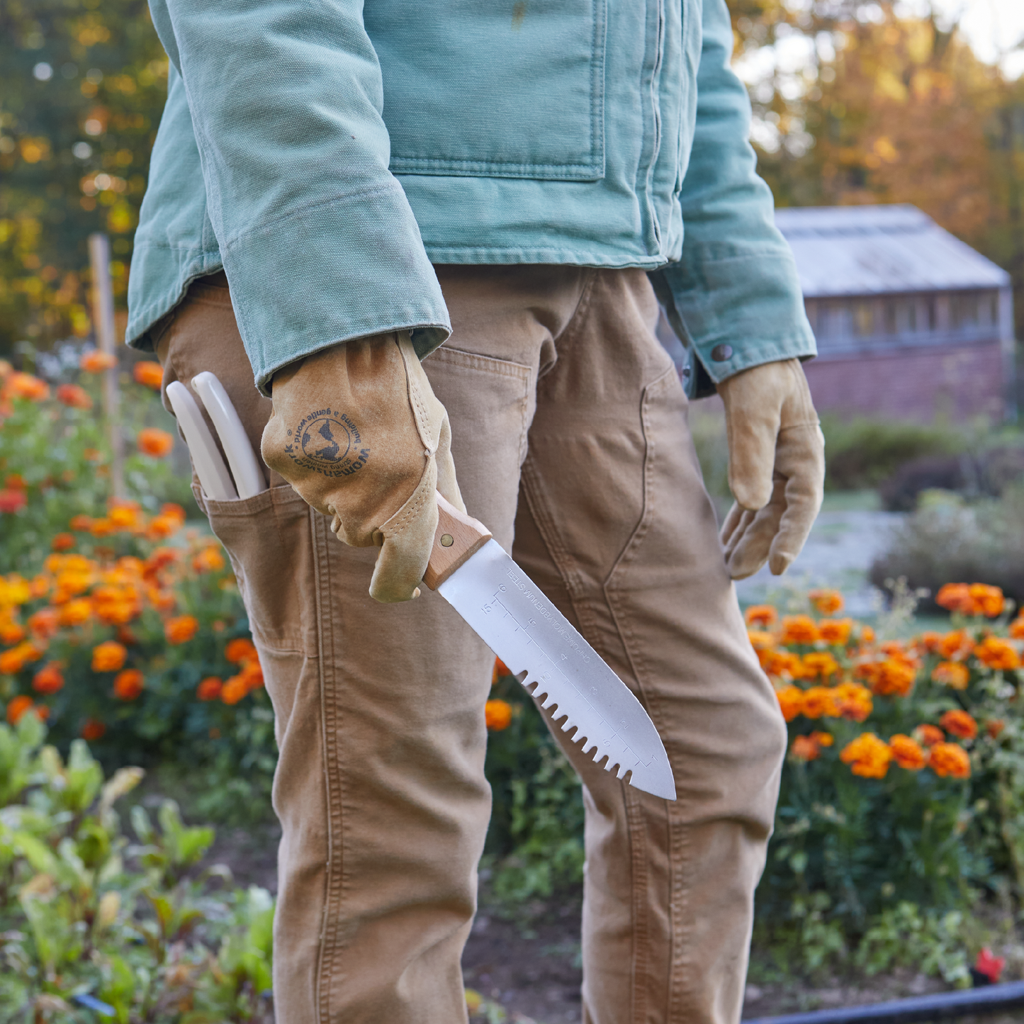 The Original Leather Work Glove by Womanswork, tan leather with logo, gardener in denim jacket in a flower garden on Tampa Home & Garden Store