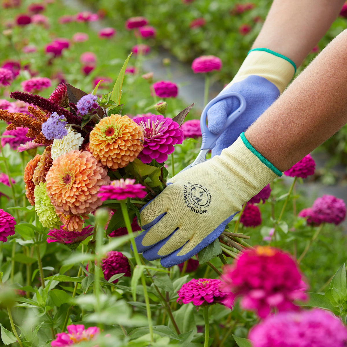 The Weeder Glove by Womanswork, cream-yellow glove with blue palm, in a colorful flower garden on Tampa Home & Garden Store