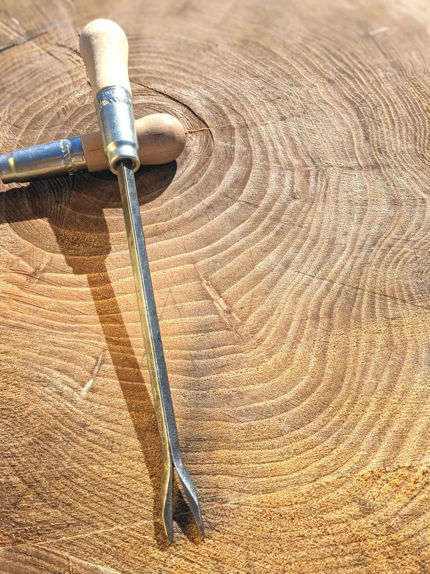 Weeding fork with wooden handle and steel two-prong tines on a textured wooden log background on Tampa Home & Garden Store