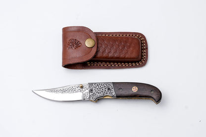 Hand-engraved folding knife with Damascus scrollwork, dark wood handle, leather sheath on Tampa Home & Garden Store