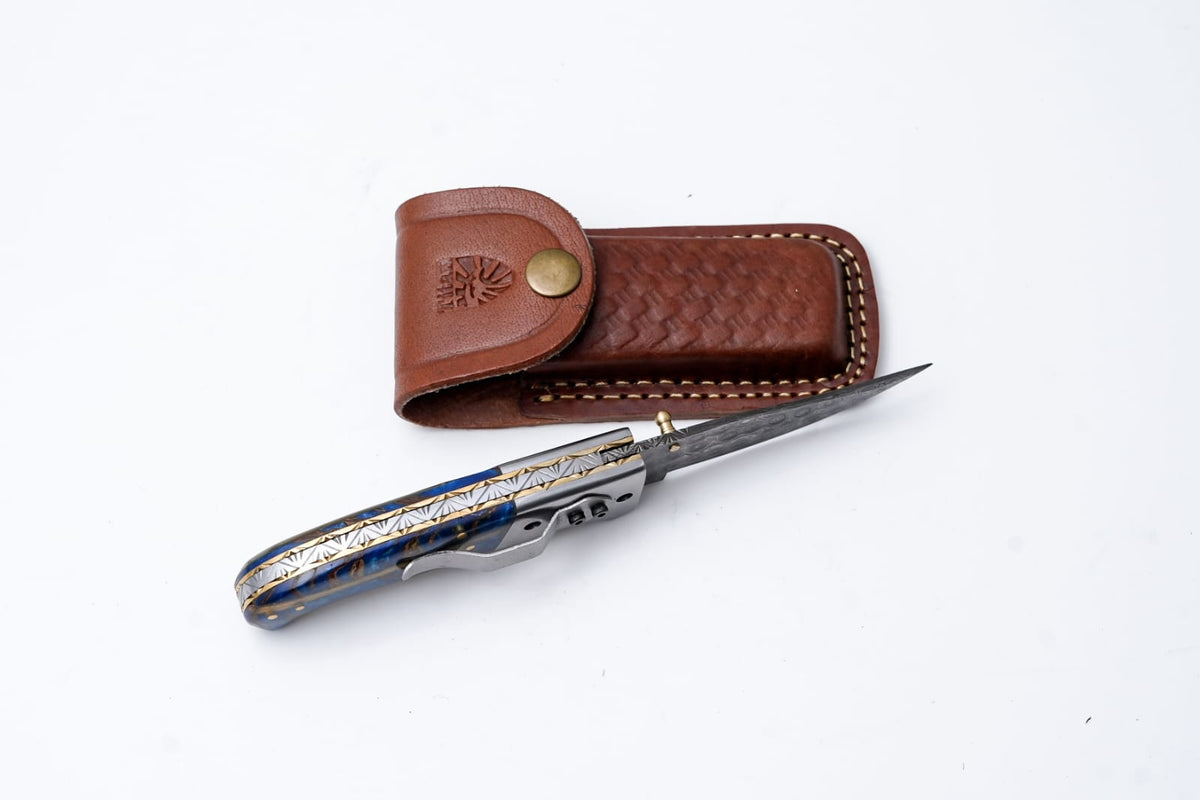 Hand-engraved folding knife with Damascus-inspired blade and brown leather sheath by Titan K on Tampa Home & Garden Store