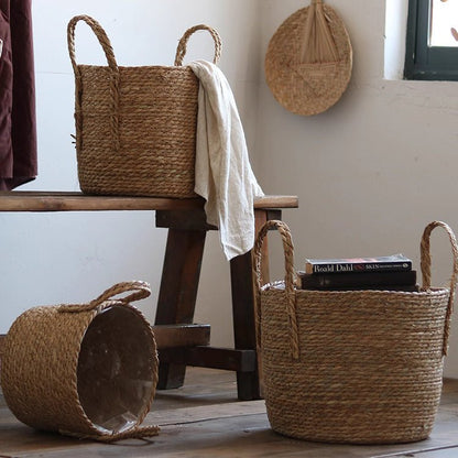 Three handwoven seagrass plant baskets in natural tan with handles, towel on bench and books on Tampa Home & Garden Store