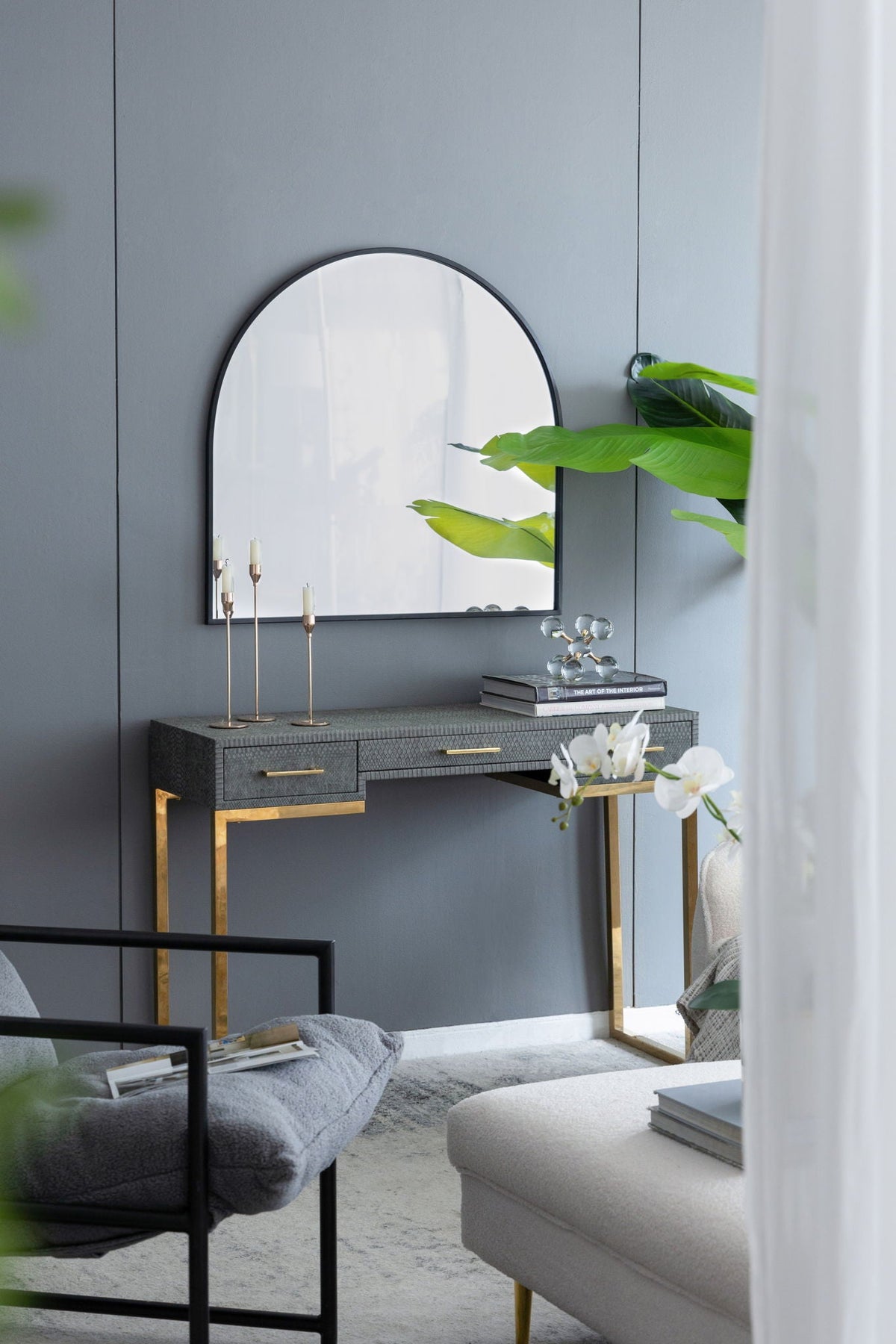 Arched wall mirror with black metal frame on blue wall above a textured dark console table on Tampa Home & Garden Store