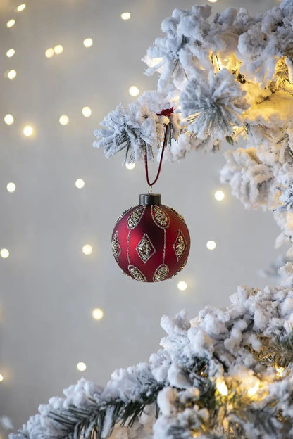 Christmas ball ornament, red with gold glitter diamond pattern, hanging on snowy branch on Tampa Home & Garden Store
