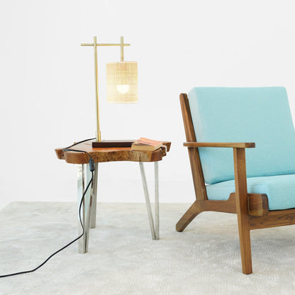 Bronze bedroom table lamp with woven shade on a wooden side table beside a turquoise chair on Tampa Home & Garden Store