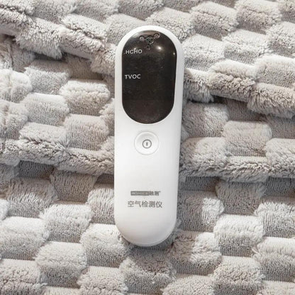 White handheld air quality detector with black display shows HCHO and TVOC on beige sofa cushion on Tampa Home & Garden Store