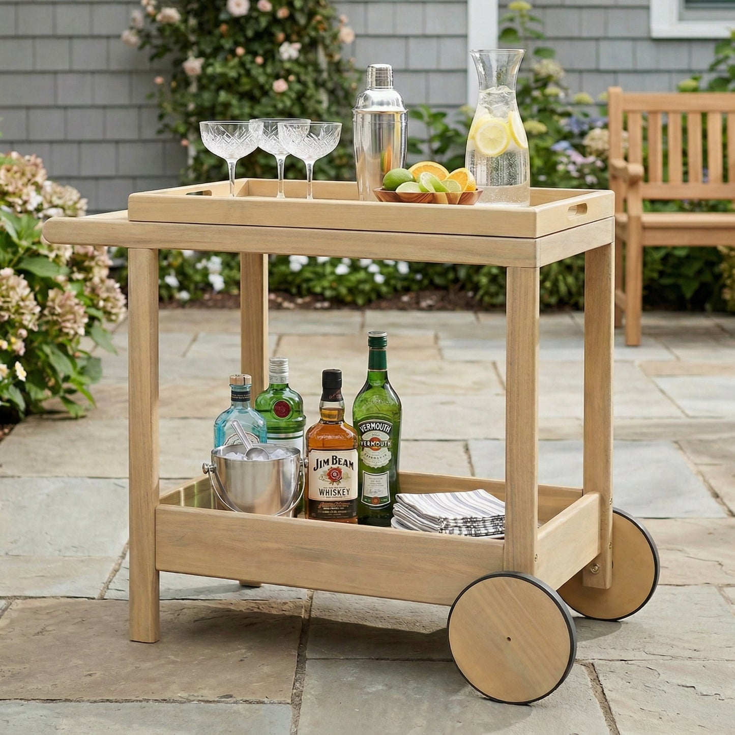 Saratoga Outdoor Rolling Bar Cart in natural wood finish with wheels, liquor bottles and glassware on Tampa Home & Garden Store
