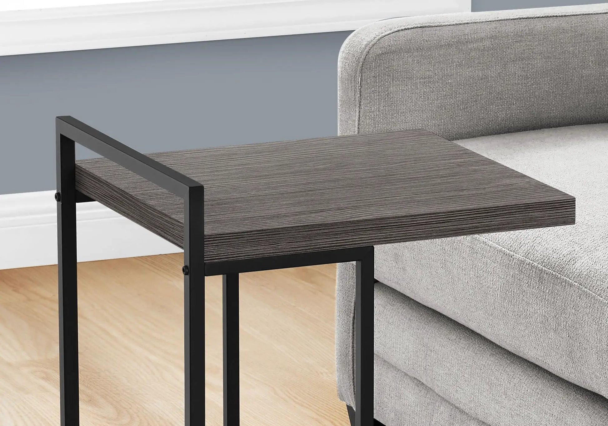 Accent table, C-shaped with dark wood grain top and black metal frame beside a gray sofa on Tampa Home & Garden Store