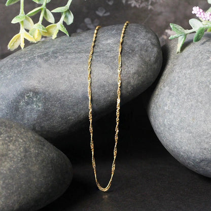 14k yellow gold Singapore chain necklace 1.5mm with twisted links displayed on grey stones on Tampa Home & Garden Store