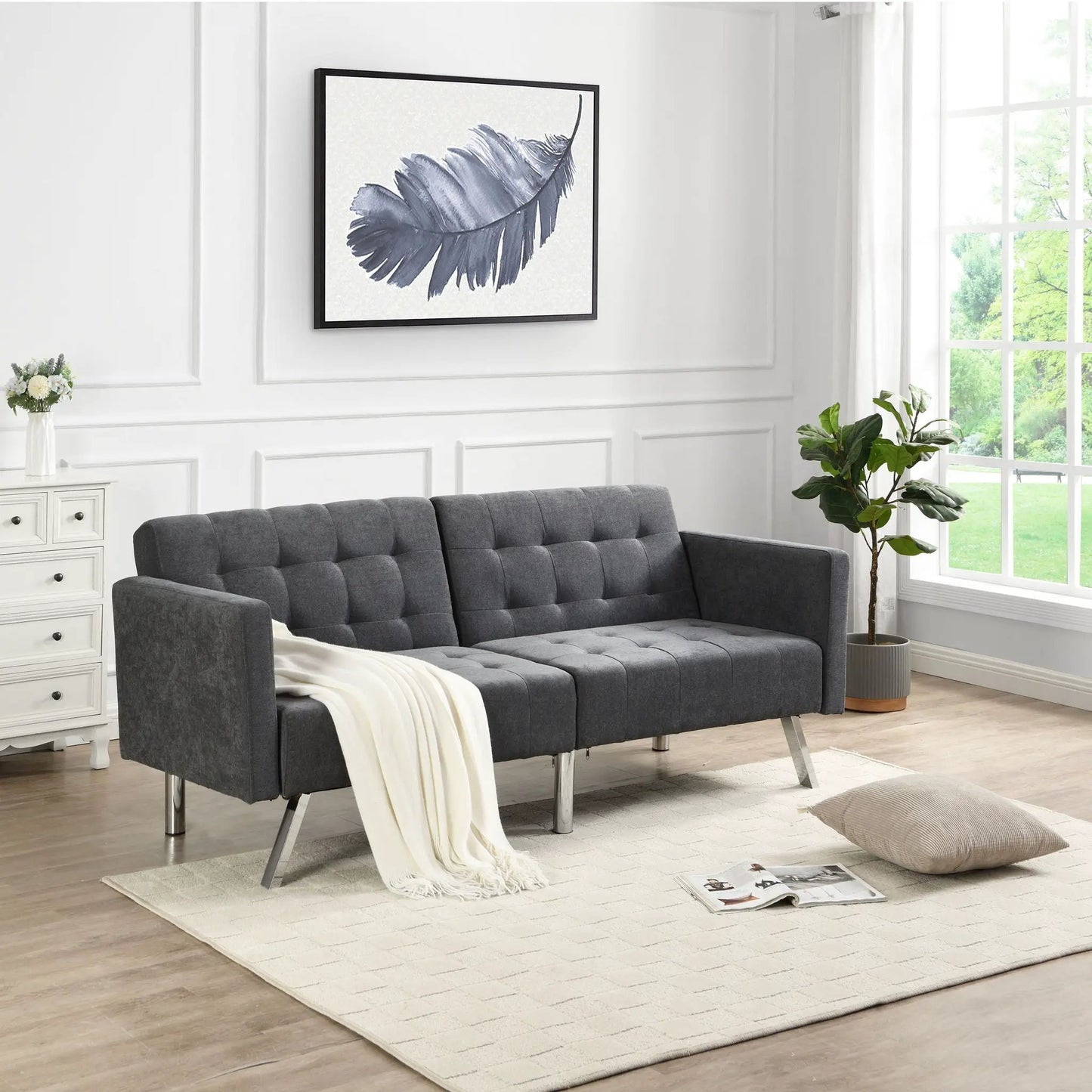 Futon sofa bed with armrests in gray tufted fabric and metal legs in a bright living room on Tampa Home & Garden Store