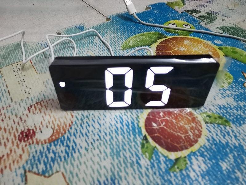 Black acrylic mirror LED alarm clock with large white digits on a bedside table on Tampa Home & Garden Store
