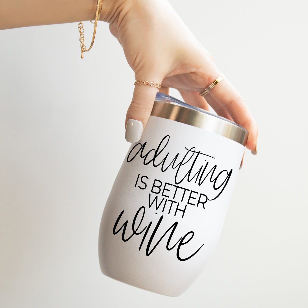 Adulting 17oz tumbler by Gia Roma, white matte finish with metallic lid, features the script adulting is better with wine, hand holding on Tampa Home & Garden Store