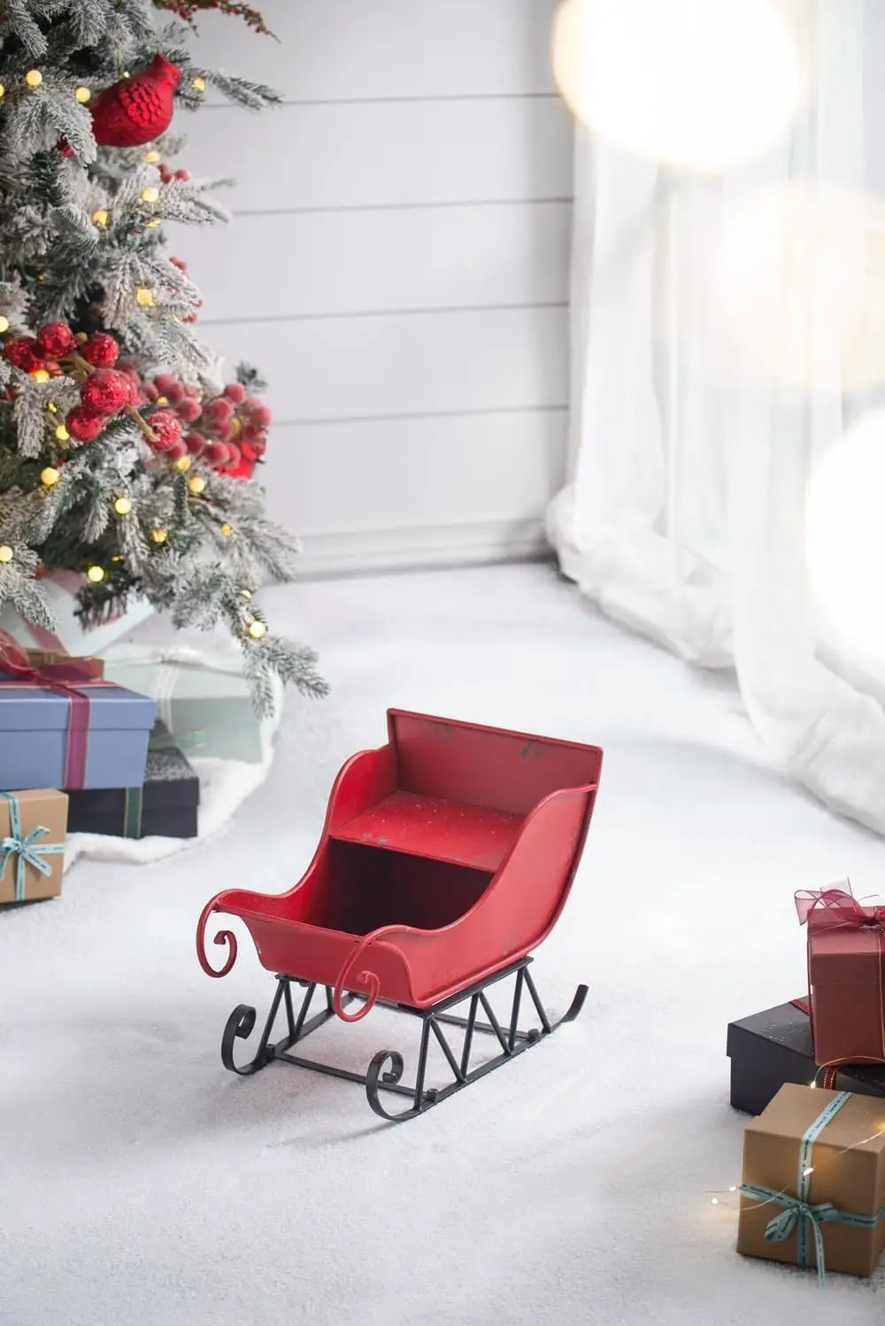 Large distressed red iron Santa sleigh holiday decoration on snowy floor beside gifts on Tampa Home & Garden Store