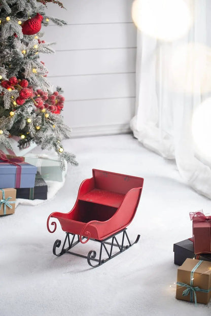 Large distressed red iron Santa sleigh holiday decoration on snowy floor beside gifts on Tampa Home & Garden Store