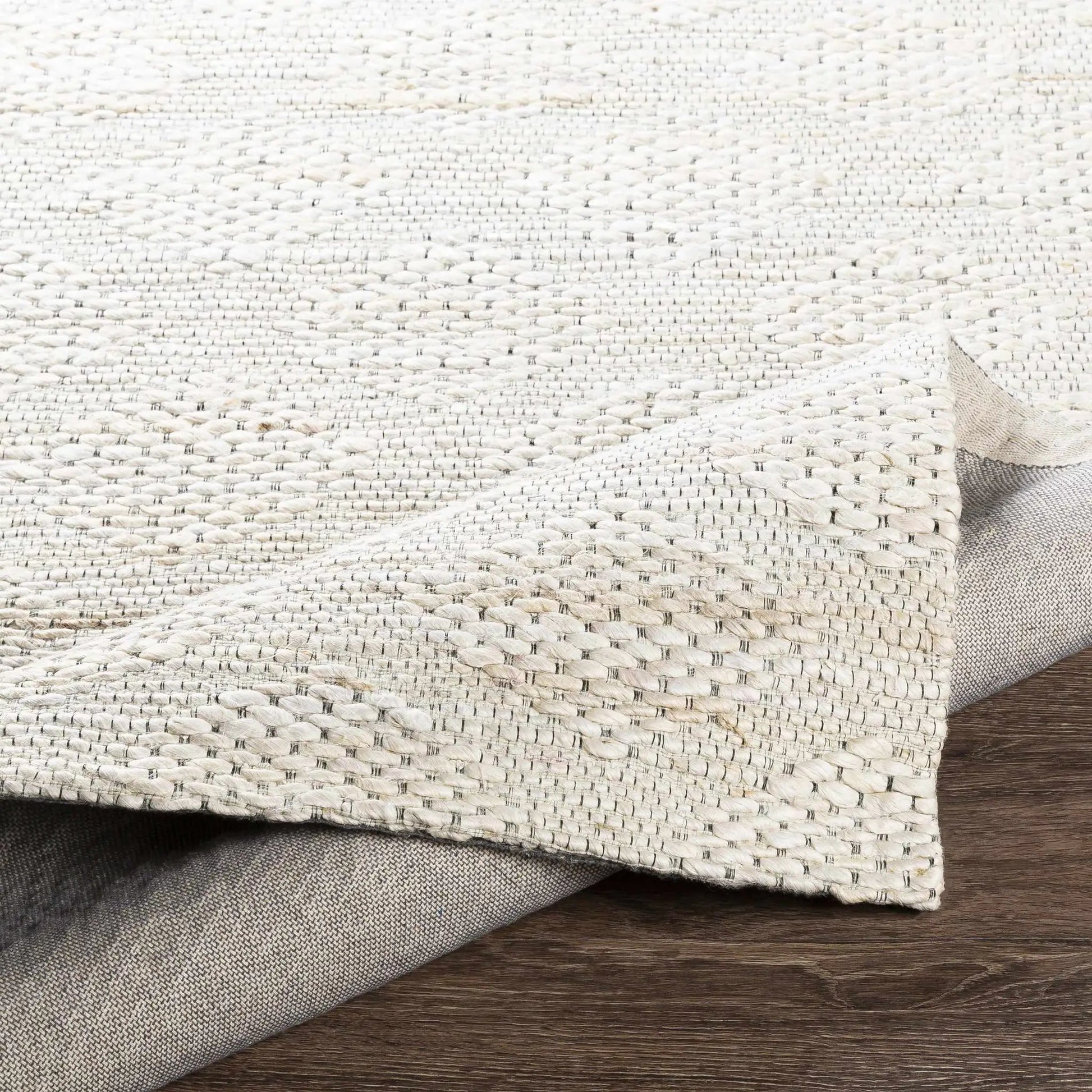 Angaston Beige Jute Rug by Boutique Rugs, beige textured rug rolled and stacked on wood floor on Tampa Home & Garden Store