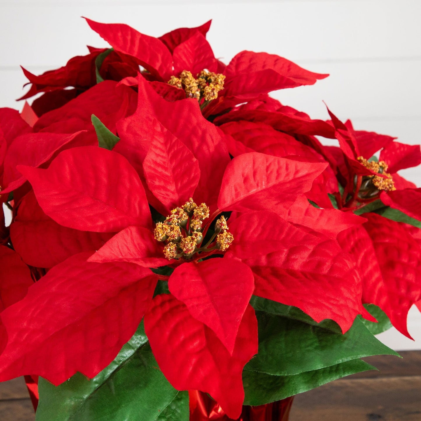 Artificial poinsettia arrangement with red bracts, green leaves, in a red wrapped planter on Tampa Home & Garden Store