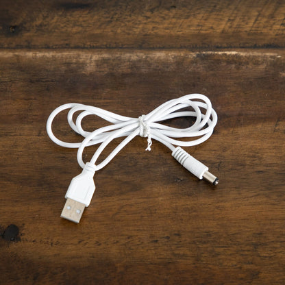 White USB power cable with USB-A plug and DC barrel connector coiled on a wooden surface on Tampa Home & Garden Store