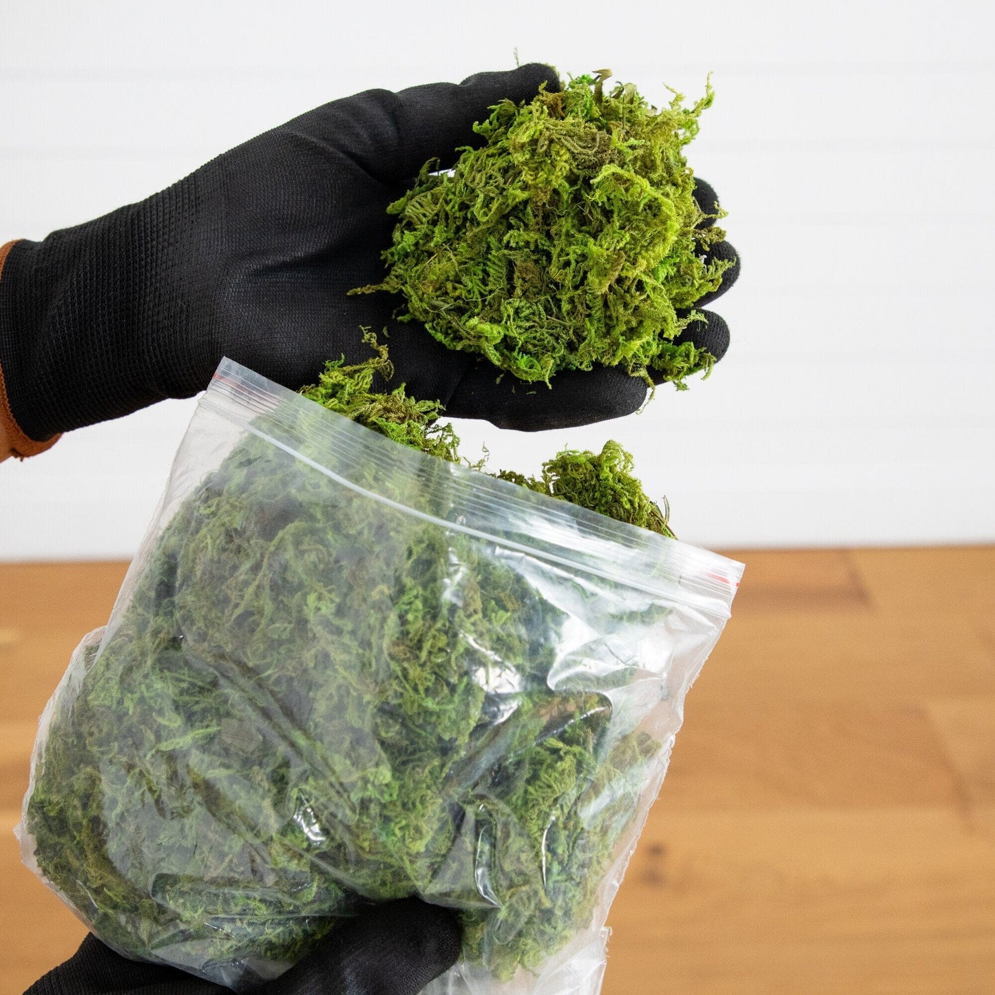 Green artificial moss bundle in a plastic bag held by gloved hand on Tampa Home & Garden Store
