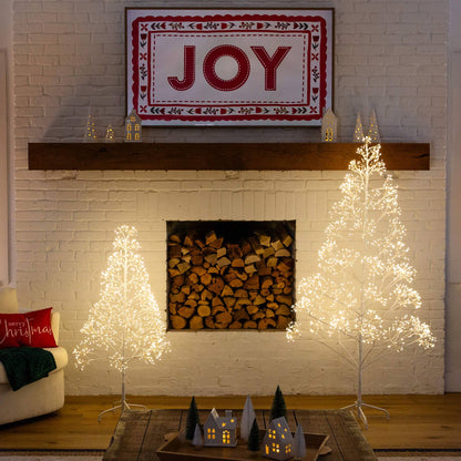 Two white starburst LED decorative trees beside a JOY sign on a brick fireplace with tiny houses on Tampa Home & Garden Store