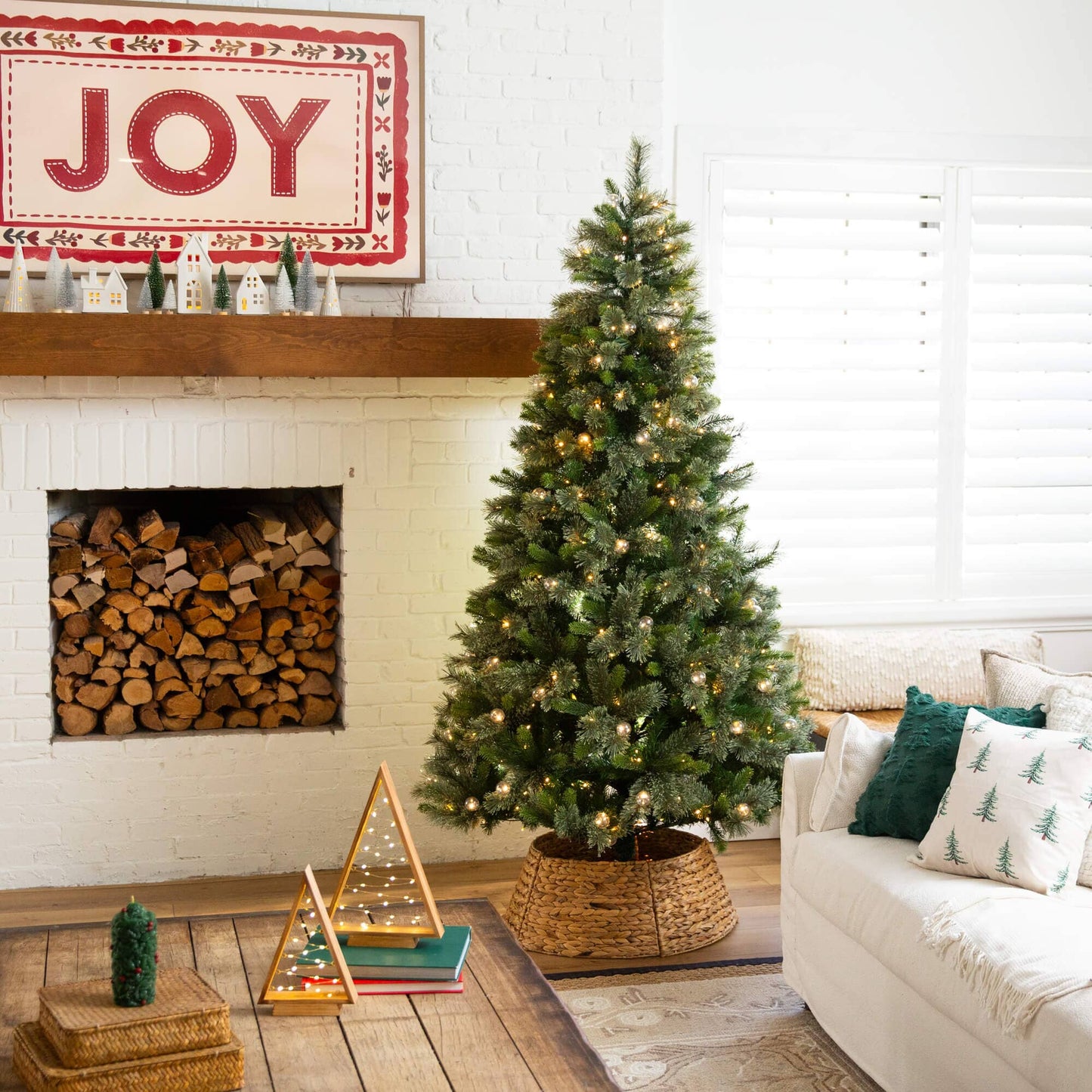 Nearly Natural 7.5' artificial Christmas tree with 450 warm white globe bulbs and LED lights, placed in a cozy living room beside a white brick fireplace on Tampa Home & Garden Store