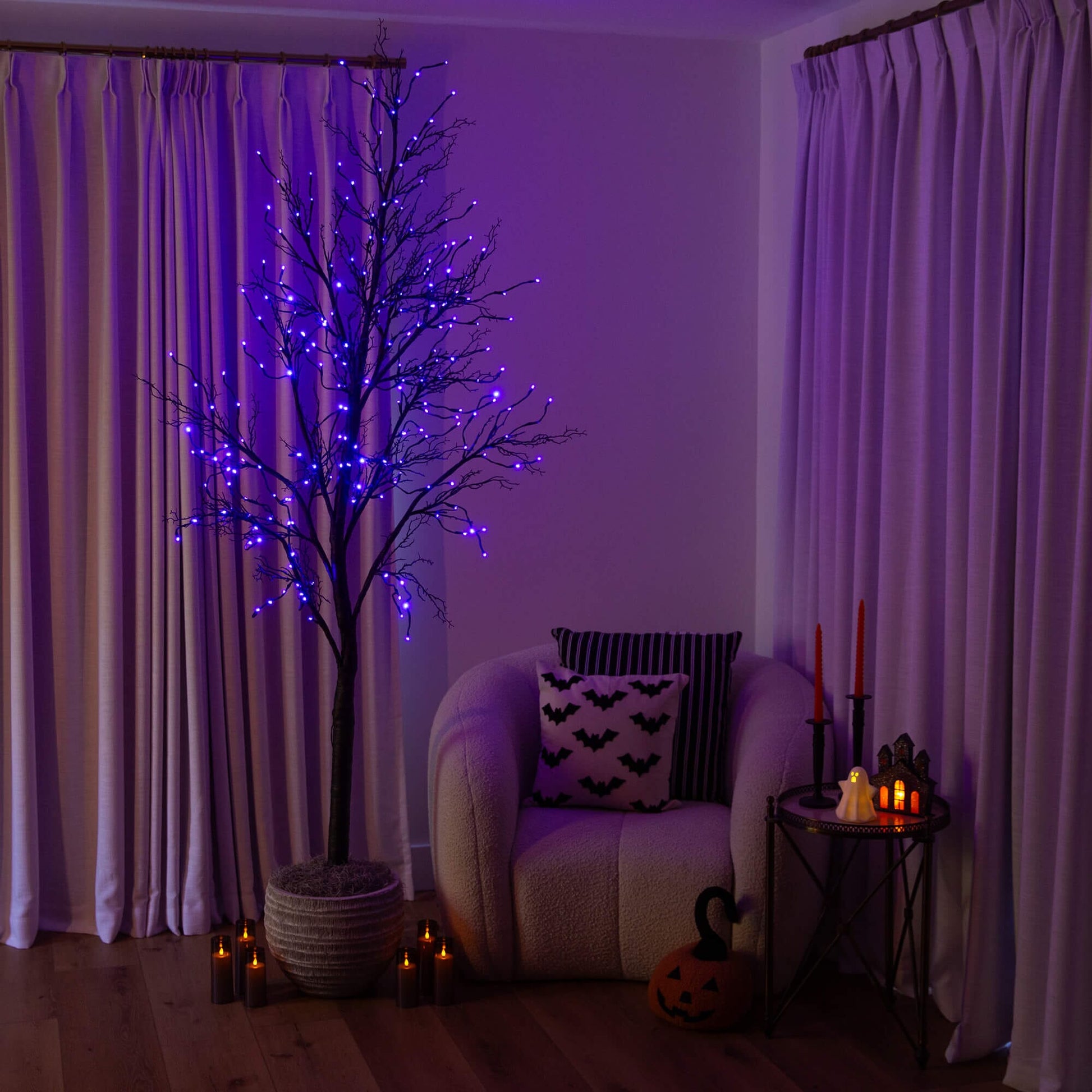 8' Pre-Lit Halloween Deluxe Black Twig Artificial Tree with 216 Orange & Purple LED Lights in a dim living room on Tampa Home & Garden Store