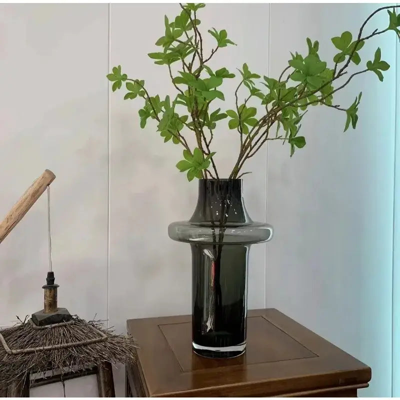 Amber glass bulbous vase with a ringed neck holding green leafy stems on a wooden table on Tampa Home & Garden Store