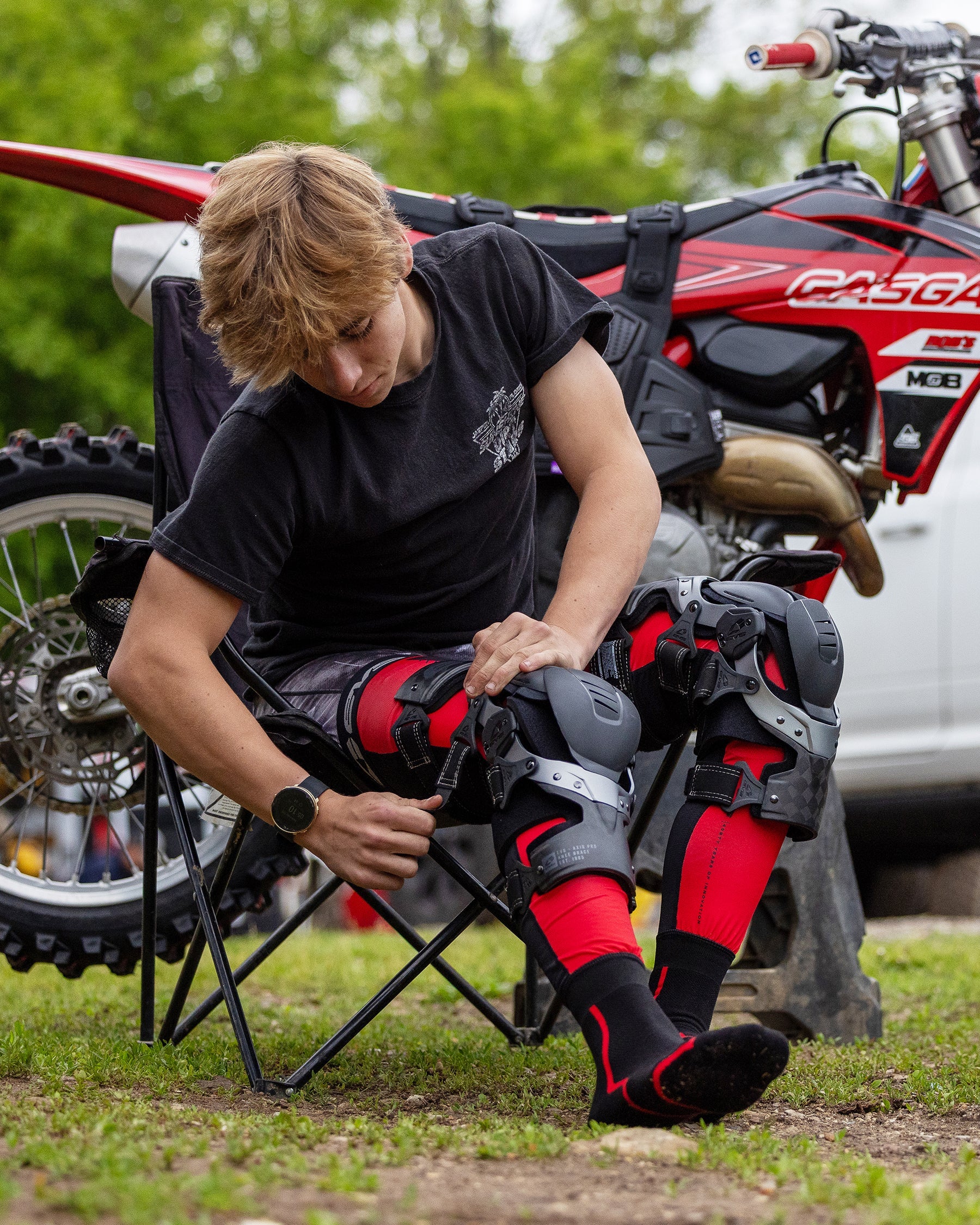 EVS Axis Pro 2025 knee brace, red/black with gray hinges, worn by rider beside a red dirt bike on Tampa Home & Garden Store