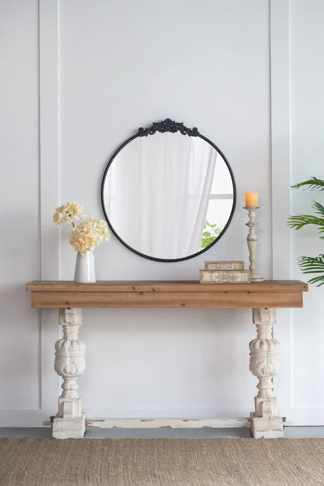 Round wall mirror with a black Baroque-inspired ornate frame leaning on a wooden console on Tampa Home & Garden Store