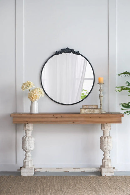 Round wall mirror with a black Baroque-inspired ornate frame leaning on a wooden console on Tampa Home & Garden Store