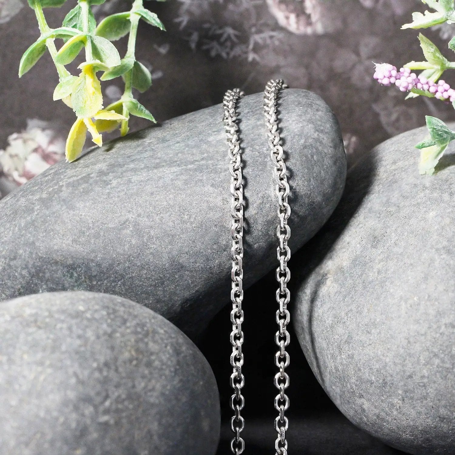 Two 14k white gold diamond-cut cable link chains draped over smooth rocks on Tampa Home & Garden Store